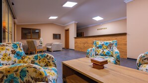 A reception area with a wooden reception desk, floral armchairs, a wooden coffee table, and a seating area with a sofa and chairs. - Dream Holiday Resort  (Burhaniye)