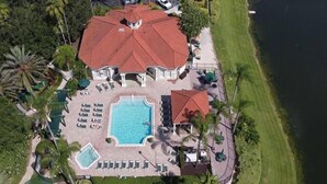 An aerial view of a resort with a large swimming pool, multiple lounge areas, and a red-roofed building. - 4BR Resort Home, 2 King Suites. Disney 9 min. Pools/Tennis/Pickleball/Gym/Sauna (Kissimmee)