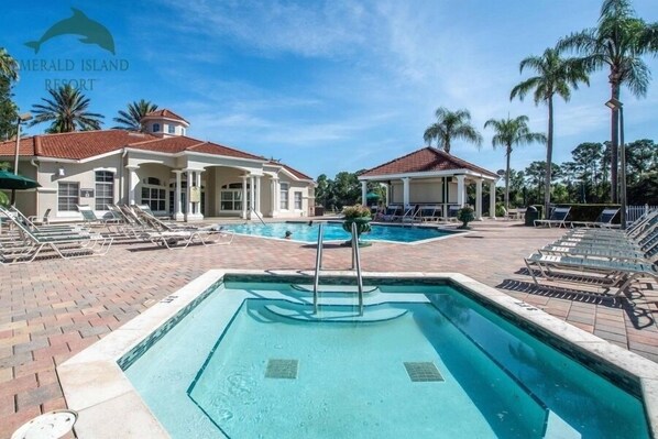 A resort with a swimming pool, lounge chairs, and palm trees.