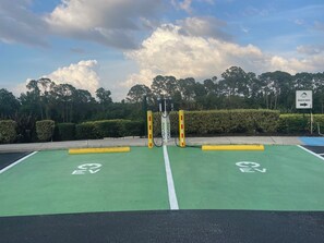 A green EV charging station with a sign indicating a beach area to the right. - 4BR Resort Home, 2 King Suites. Disney 9 min. Pools/Tennis/Pickleball/Gym/Sauna (Kissimmee)