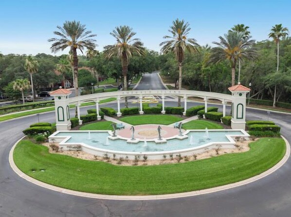 A landscaped area with a fountain, palm trees, and a white archway.