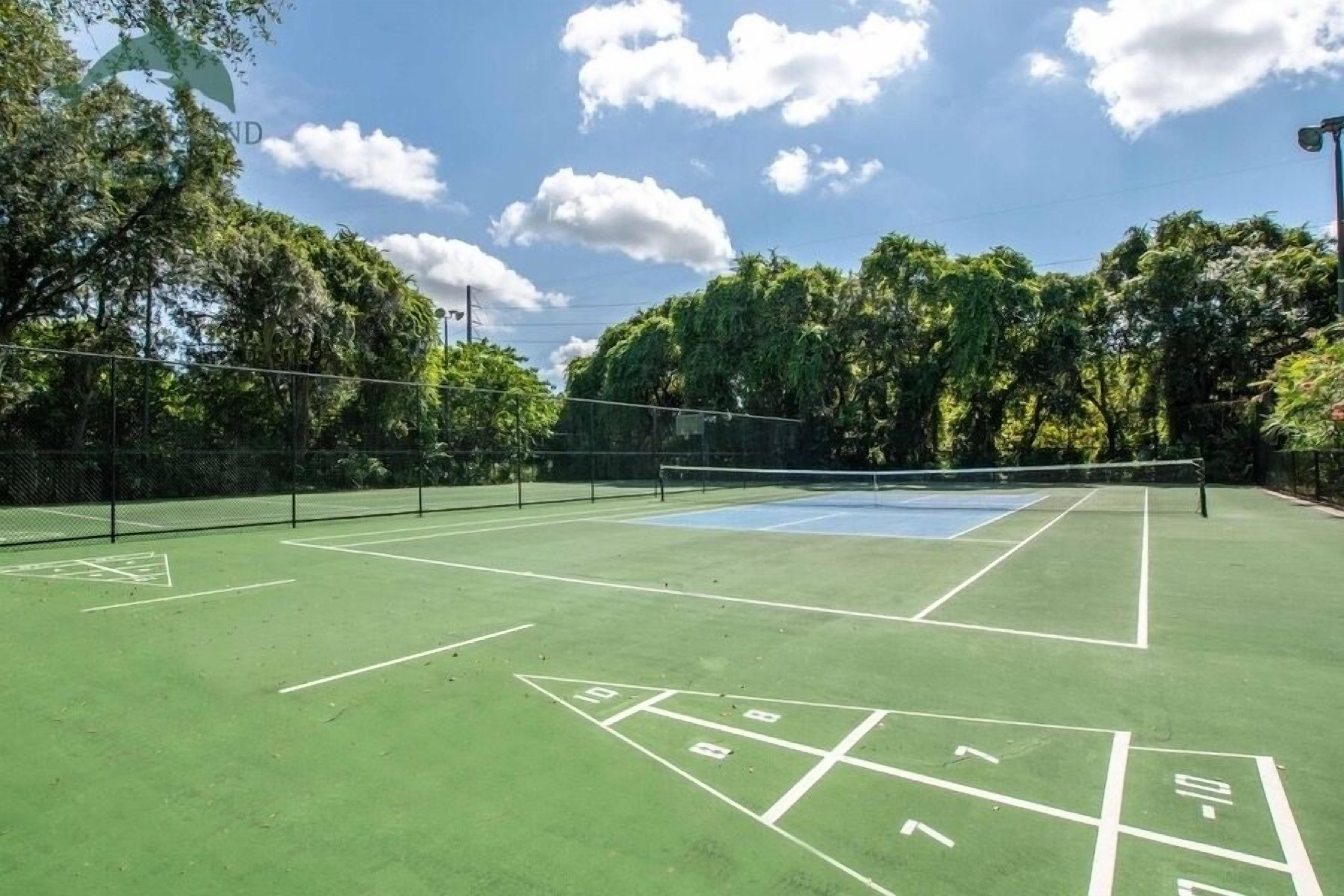 An outdoor tennis court with a net, surrounded by trees and a clear sky.