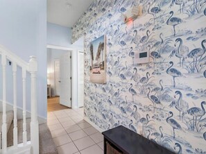 Un pasillo con papel tapiz decorativo, una escalera y una consola.