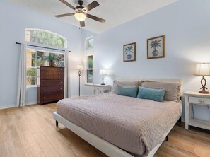 A bedroom with a bed, a dresser, a nightstand, a ceiling fan, and two wall-mounted lamps. - 4BR Resort Home, 2 King Suites. Disney 9 min. Pools/Tennis/Pickleball/Gym/Sauna (Kissimmee)