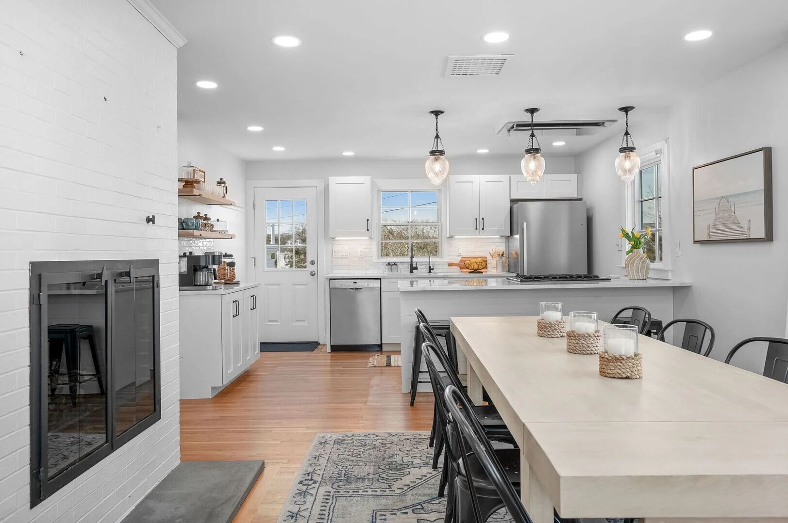 A modern kitchen with white cabinetry, a stainless steel refrigerator, and pendant lighting.