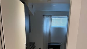 Ein schmaler Flur mit einer Küchenzeile links, einem Esstisch mit Stühlen in der Mitte und einem Fenster mit Vorhängen rechts.