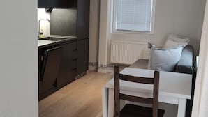 Ein kompakter Wohnbereich mit Küchenzeile, einem Essbereich mit Tisch und Stühlen sowie einem Fenster mit Jalousien.