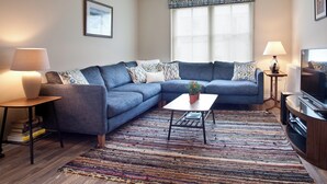 A living room with a sectional sofa, a coffee table, a television, and a patterned rug. - Mackay Road - UK7451 (Dornoch)