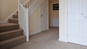 A staircase with carpeted steps and white railings leading to a door with a radiator below. - Mackay Road - UK7451 (Dornoch)