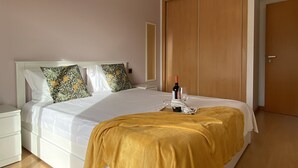 Ein ordentlich bezogenes Bett mit einem weißen Kopfteil, einer senfgelben Decke und einer Weinflasche auf dem Nachttisch.