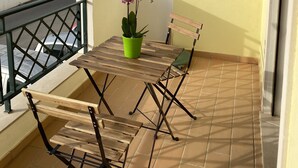Ein Balkon mit Holztisch und Stühlen, einem Blumentopf und Blick auf die Stadt.