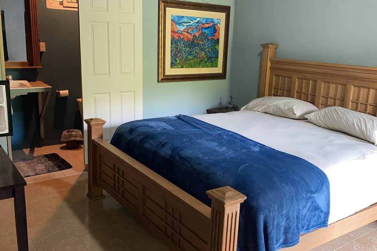 A bedroom with a wooden bed, a nightstand, a desk, and a painting on the wall.