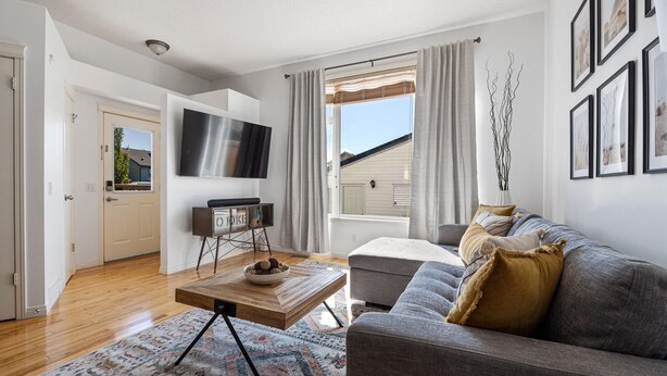 A modern living room with a grey sofa, a wooden coffee table, and a flat-screen TV mounted on the wall. - Cozy Home w/ Free Parking | Fireplace & Backyard | Sleeps 8 | Near Banff (Calgary)