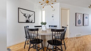 A dining area with a round table, four black chairs, a modern chandelier, and artwork on the walls. - Cozy Home w/ Free Parking | Fireplace & Backyard | Sleeps 8 | Near Banff (Calgary)