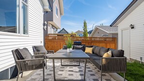A patio with a table and chairs, a sofa, and a wooden fence. - Cozy Home w/ Free Parking | Fireplace & Backyard | Sleeps 8 | Near Banff (Calgary)