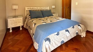 A bedroom with a wooden floor, a bed with a patterned bedspread, two bedside tables with lamps, and a wardrobe. - Aparatemento de Lujo Paramont Tucumán (Tucuman)