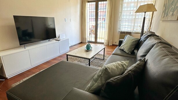 A living room with a flat-screen TV, a sofa, a coffee table, and a lamp. - Aparatemento de Lujo Paramont Tucumán (Tucuman)