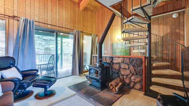 Un acogedor interior de cabaña con chimenea de piedra, una zona de estar confortable y una escalera espiral.
