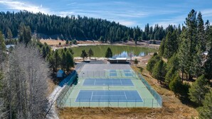 Una cancha de tenis al aire libre rodeada de árboles y un lago.
