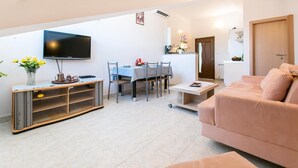 A modern living room with a flat-screen TV, a dining area with a table and chairs, and a sofa.