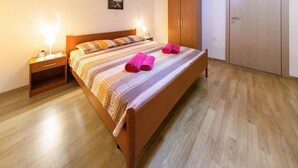 A neatly made bed with a striped bedspread and two pink towels, a wooden nightstand with a lamp, and a wooden wardrobe.