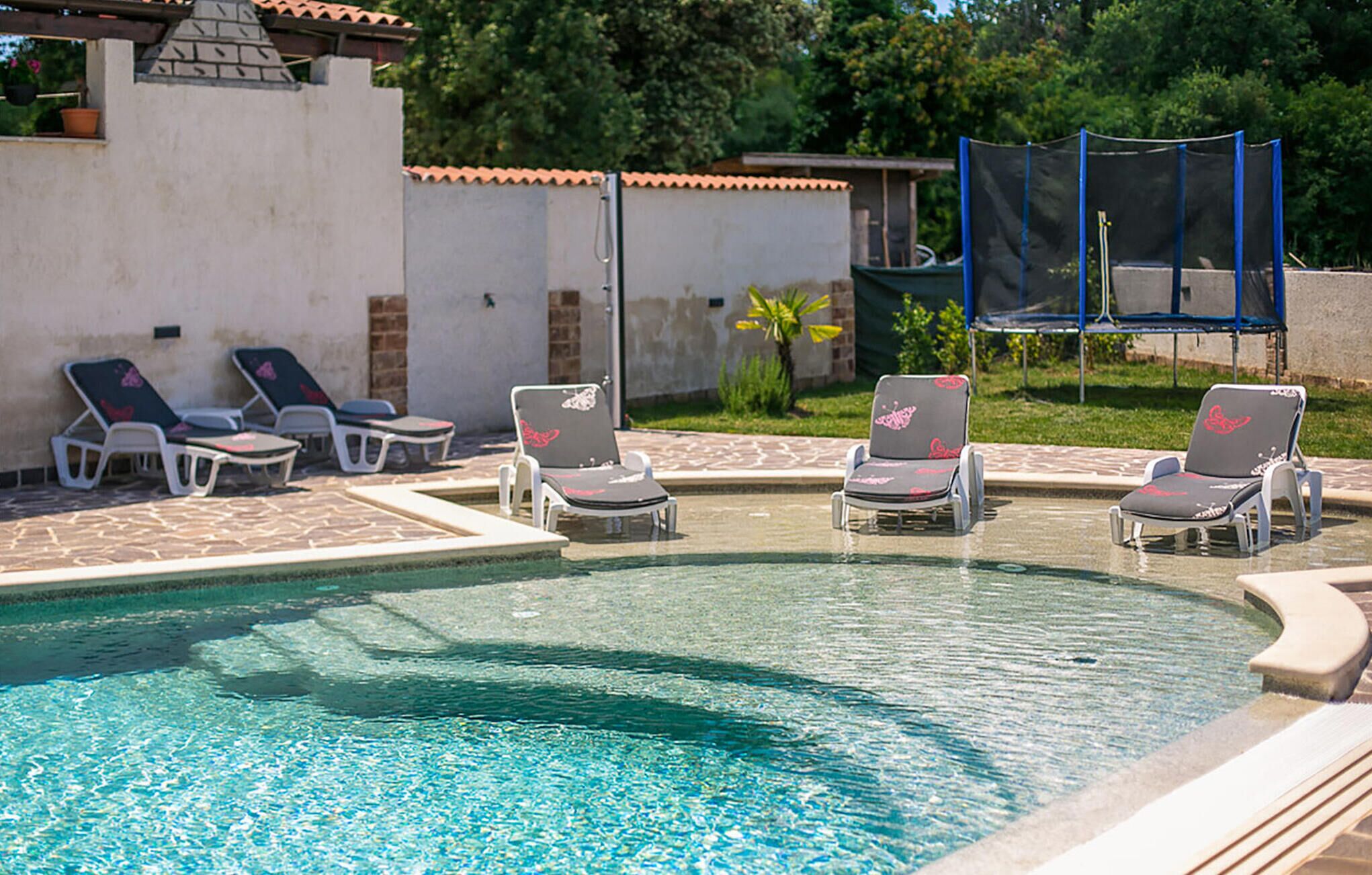 A pool area with lounge chairs and a small building with a tiled roof.