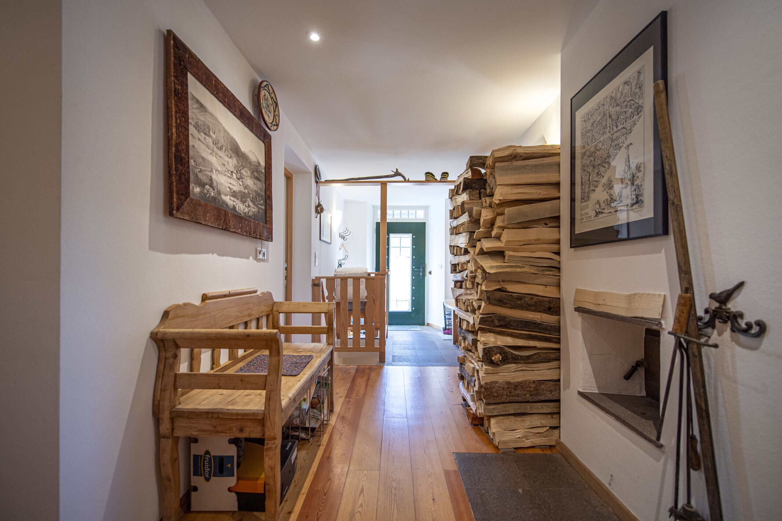 Ein Flur mit Holzbänken, einem Holzstoß und gerahmten Bildern an den Wänden.