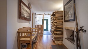 Un couloir avec des bancs en bois, une pile de bois de chauffage et des tableaux encadrés accrochés aux murs.