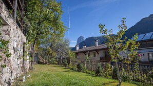 Un bâtiment en pierre avec une clôture en bois, une cour verdoyante et une montagne en arrière-plan.