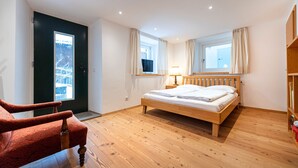 Une chambre à coucher avec un lit en bois, une chaise rouge, une fenêtre avec des rideaux et une porte donnant sur un paysage enneigé.