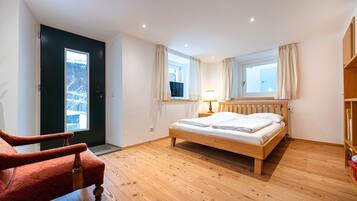 Ein Schlafzimmer mit einem Holzbett, einem roten Sessel, einem Fenster mit Vorhängen und einer Tür mit Blick auf eine verschneite Landschaft.