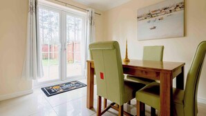 A dining area with a wooden table and four chairs, a painting on the wall, and a view through the glass door. - 3 bed house for up to 6 people In Cardiff, Wales (Cardiff)