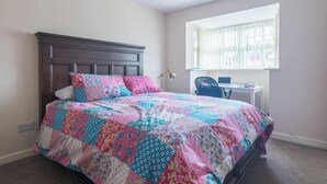 A bedroom with a dark wooden bed, a colorful quilt, a desk with a laptop, and a window with blinds. - 3 bed house for up to 6 people In Cardiff, Wales (Cardiff)