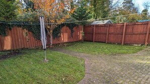 A backyard with a paved pathway, a wooden fence, and a tree with autumn leaves. - 3 bed house for up to 6 people In Cardiff, Wales (Cardiff)