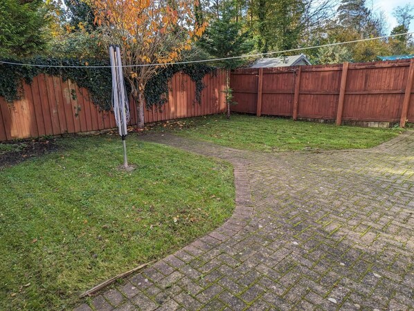 A backyard with a paved pathway, a wooden fence, and a tree with autumn leaves. - 3 bed house for up to 6 people In Cardiff, Wales (Cardiff)