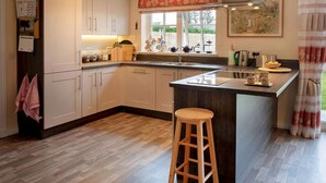 Una cocina moderna con armarios blancos, un taburete de madera y una ventana con vistas a la vegetación.
