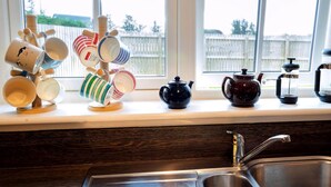 Una encimera de cocina con un juego de té, una cafetera y un colgador para tazas.