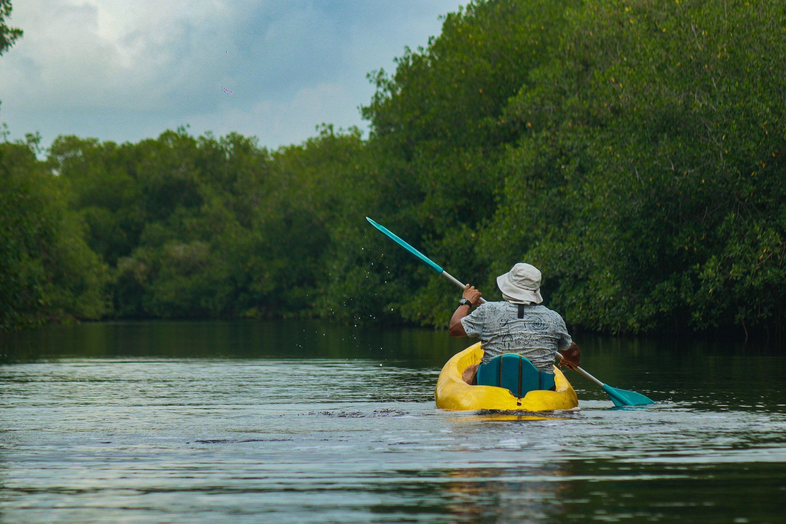 Uma pessoa num bote amarelo remando num rio calmo, rodeada por vegetação densa.