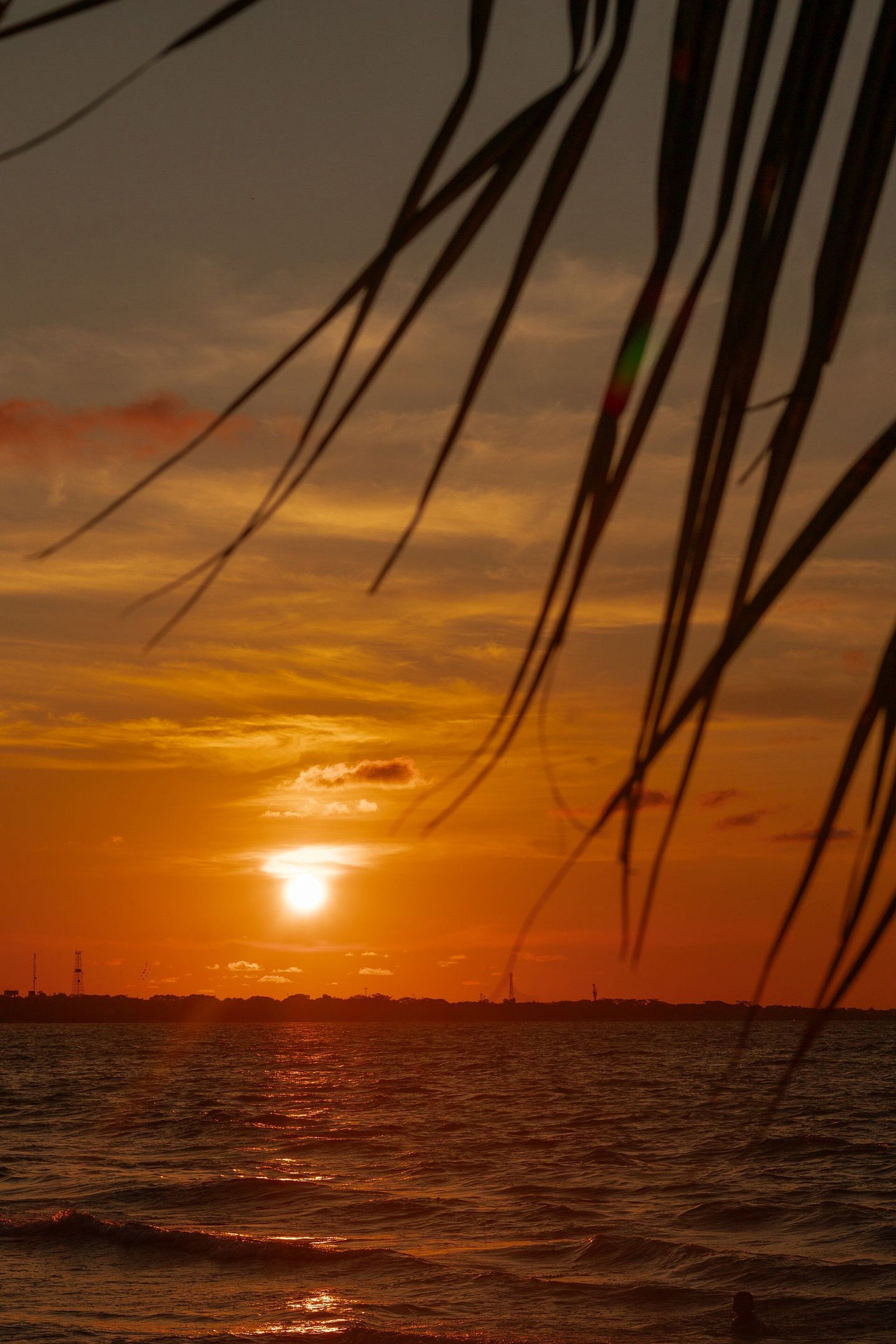 Ein Sonnenuntergang über einem Gewässer mit den Silhouetten weiter entfernter Gebäude.