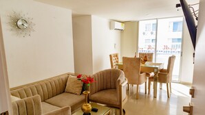 A living room with a sofa, armchairs, a glass coffee table, a decorative vase with flowers, a wall clock, and a dining area with chairs and a table. - Covenas Refugio de Familia junto al Mar (Coveñas)