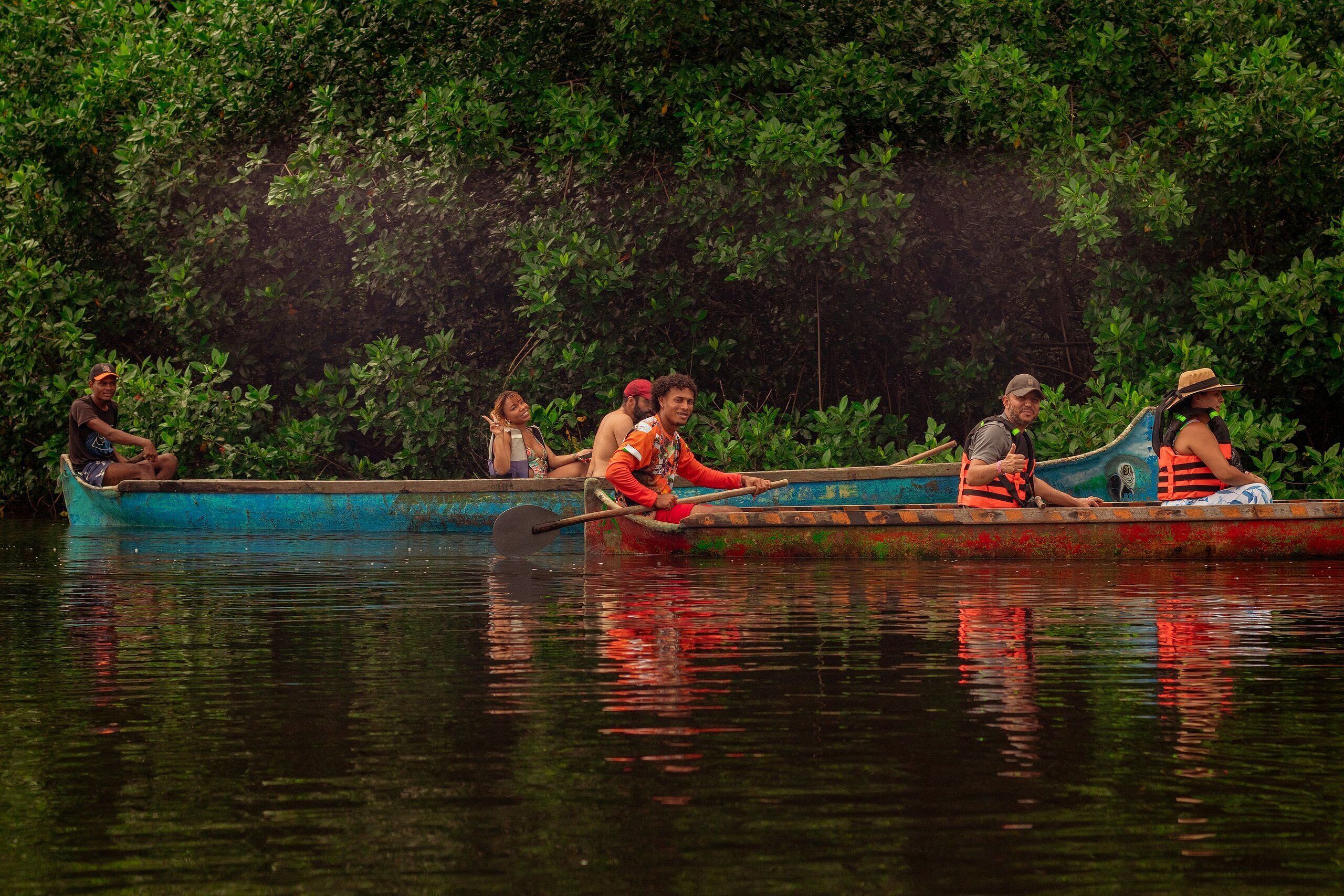 A group of people in a rowboat on a calm river surrounded by dense greenery.