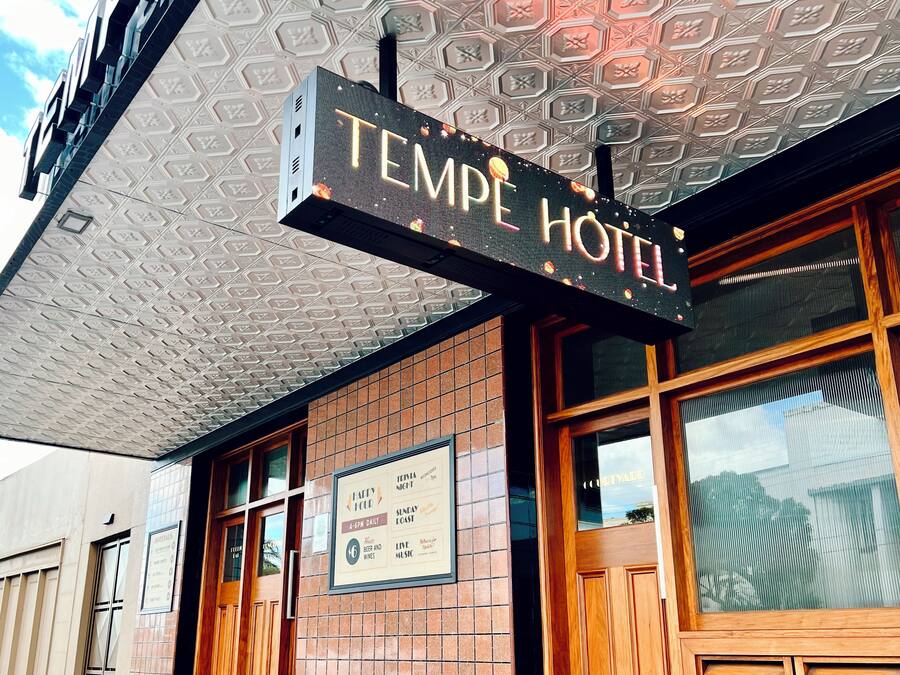 A hotel sign with the name "TEMPE HOTEL" and a sign below advertising a "FAIRY CLUB" with details like "4-6PM DAILY" and "LIVE MUSIC".