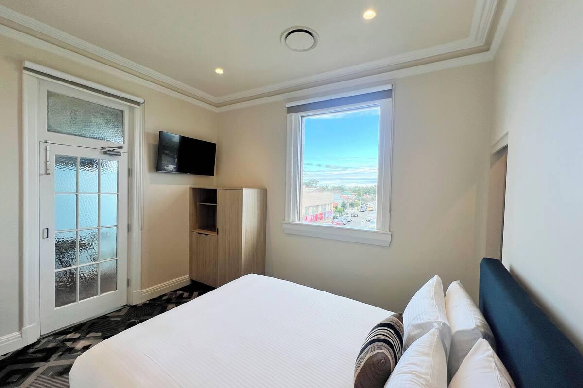 A hotel room with a bed, a television, a window with a view, and a door with frosted glass.