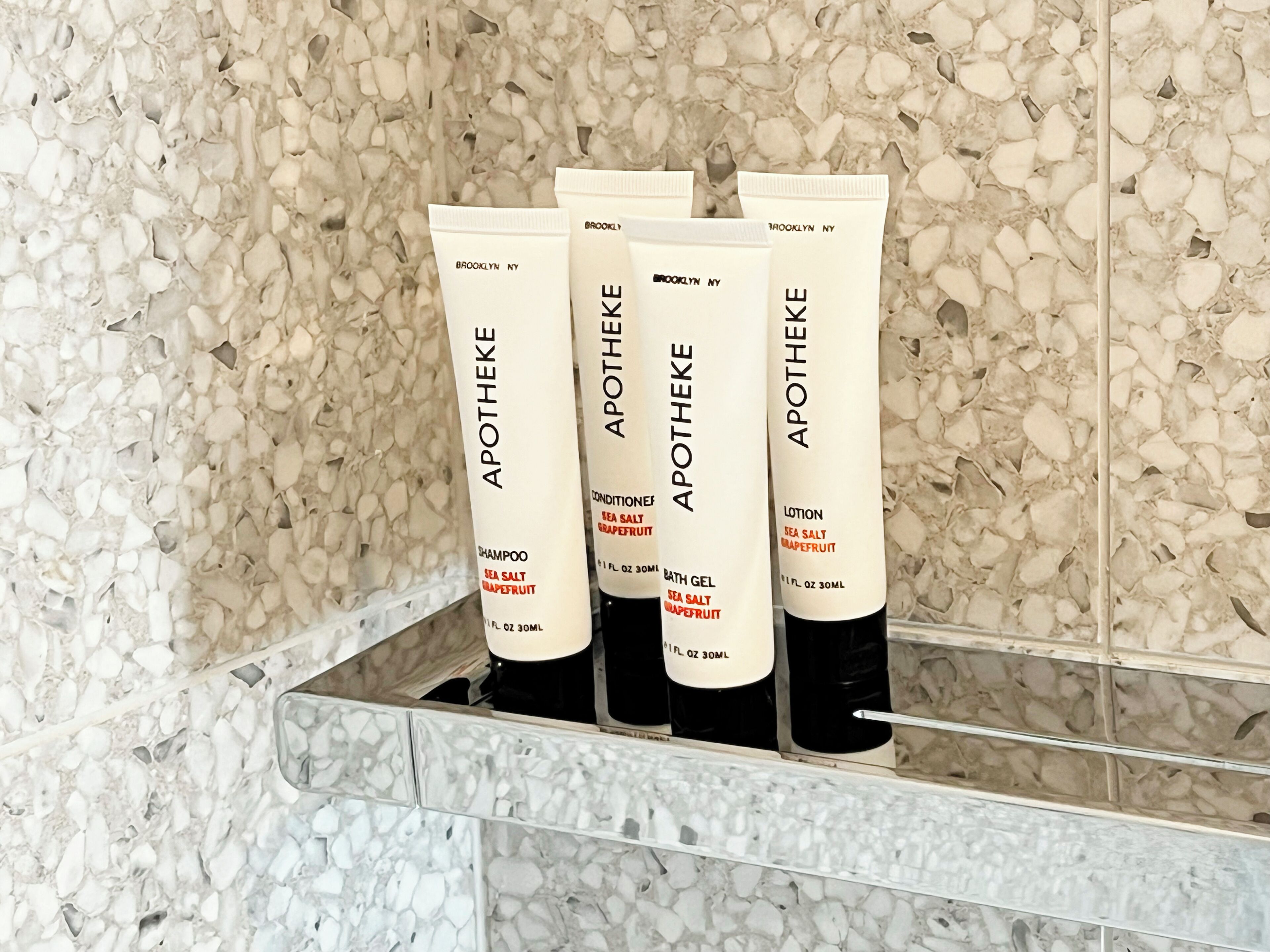 Una estantería en el baño con cuatro botellas de productos para el cuidado de la piel Apotheke.