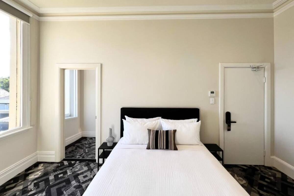 A hotel room with a large bed, a nightstand, a door, and a window.