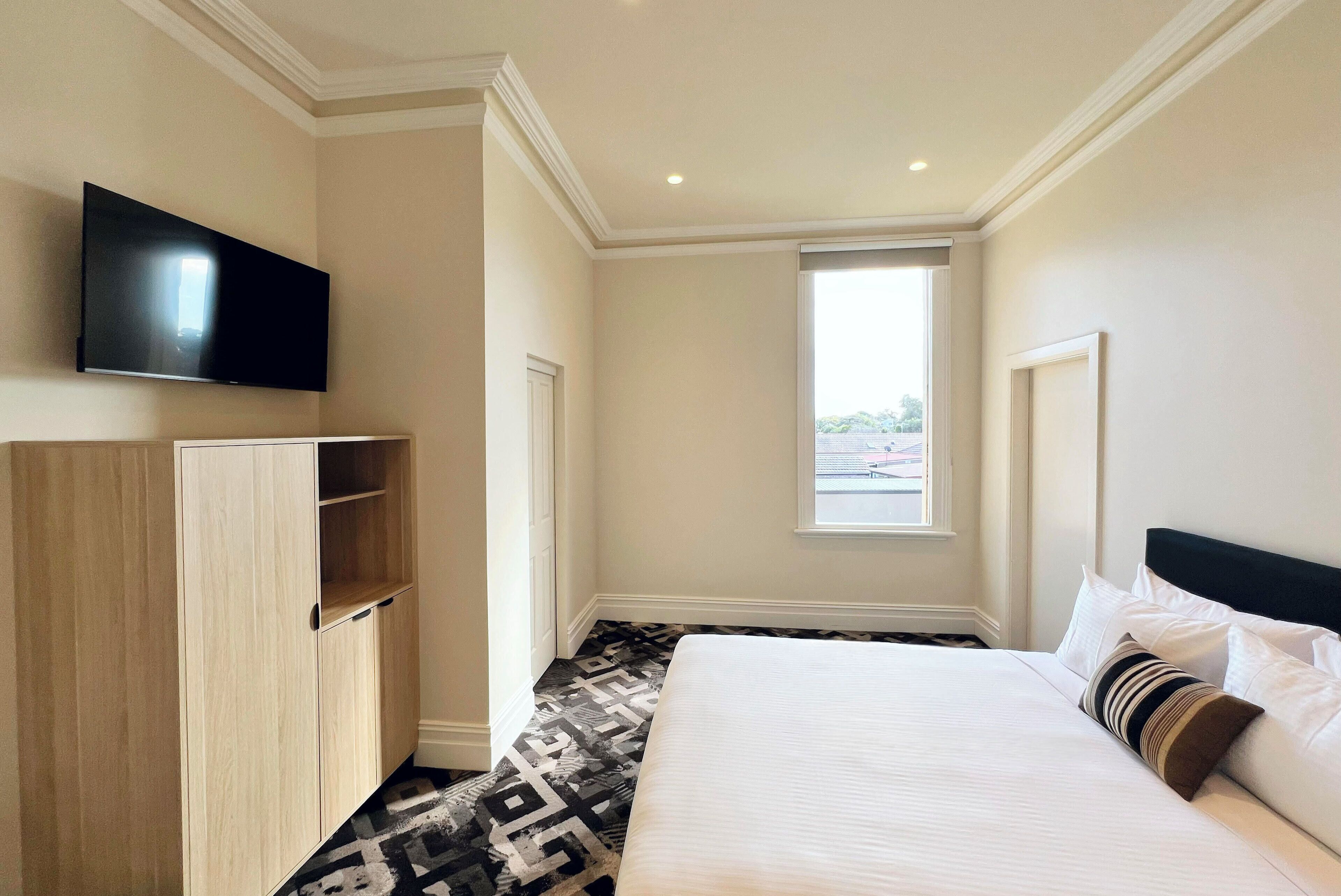 A hotel room with a large bed, a flat-screen TV mounted on the wall, and a window providing a view of the outside.