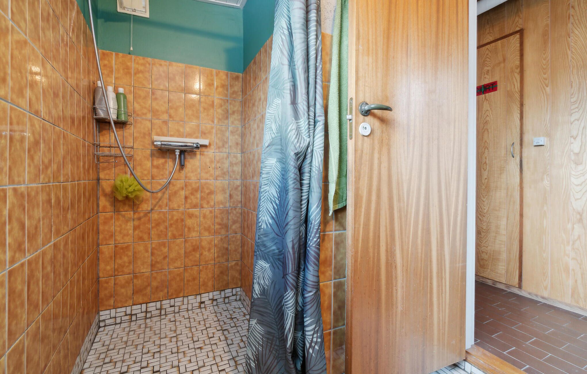 A bathroom with a shower, tiled walls, a wooden door, and a tiled floor.