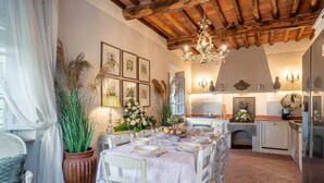 A dining area with a table set for four, surrounded by chairs, a large potted plant, and framed botanical prints on the wall.
