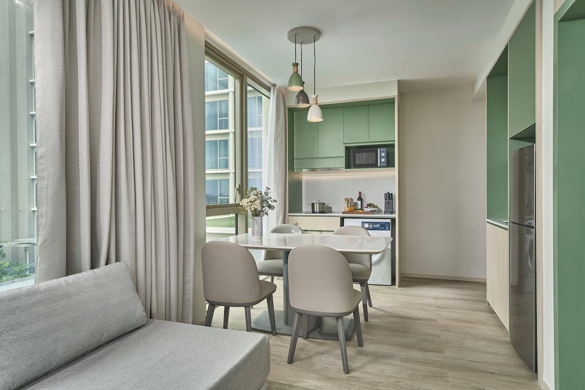 Une cuisine moderne avec des meubles de couleur verte, un coin repas avec une table et des chaises, et un canapé agrémenté d’un coussin à motifs.