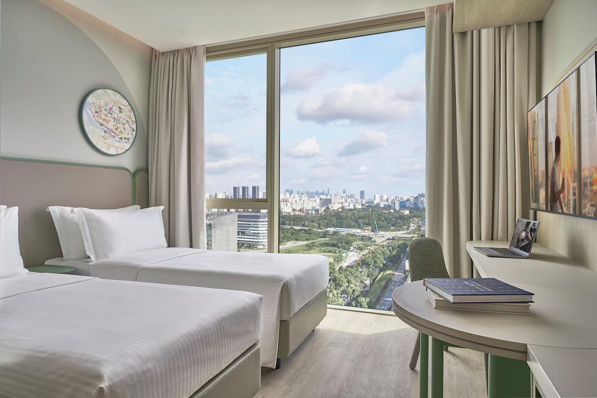 Une chambre d’hôtel avec deux lits, un bureau et une grande fenêtre donnant sur la ville.